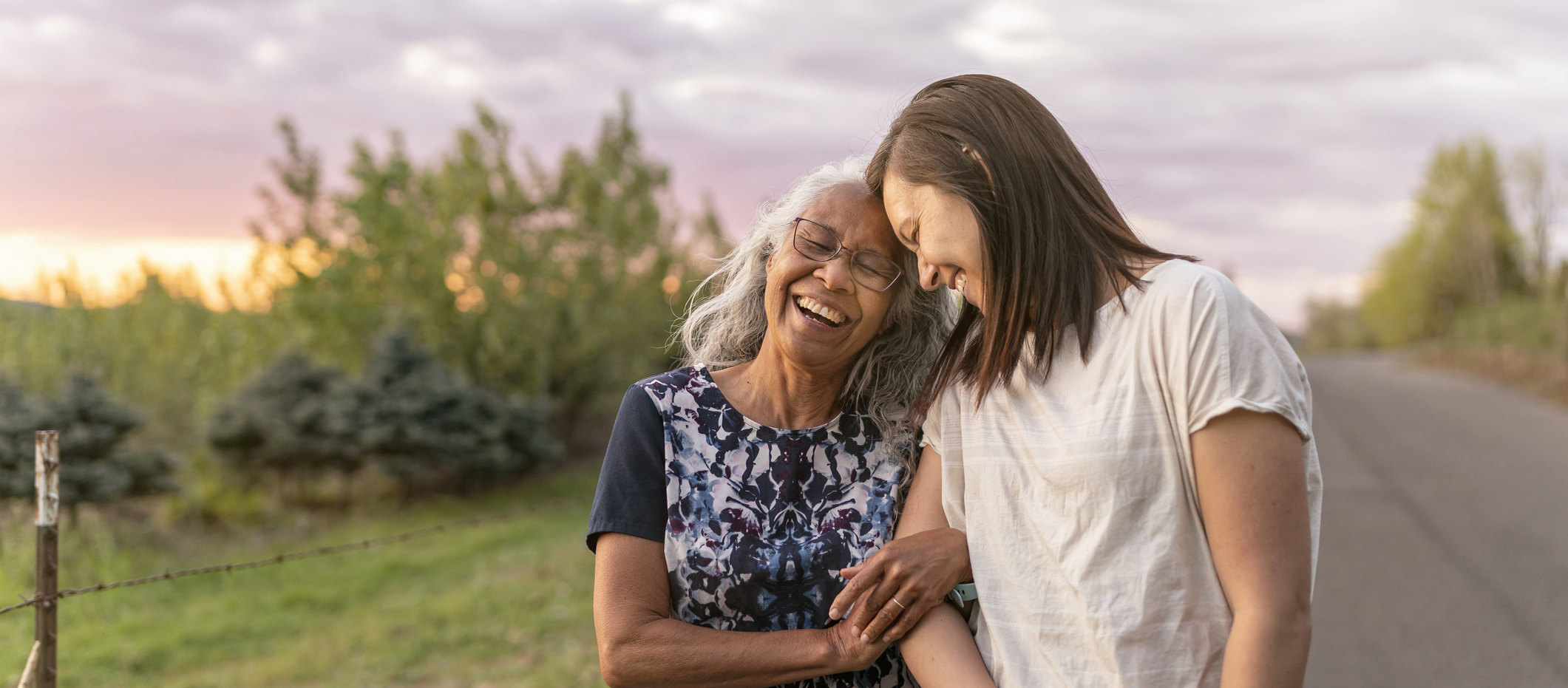 A beautiful senior mom of pacific island descent is walking outdoors with her adult thirty something year old daughter. They are enjoying each others company and soaking in the gorgeous, colorful, sunset.
